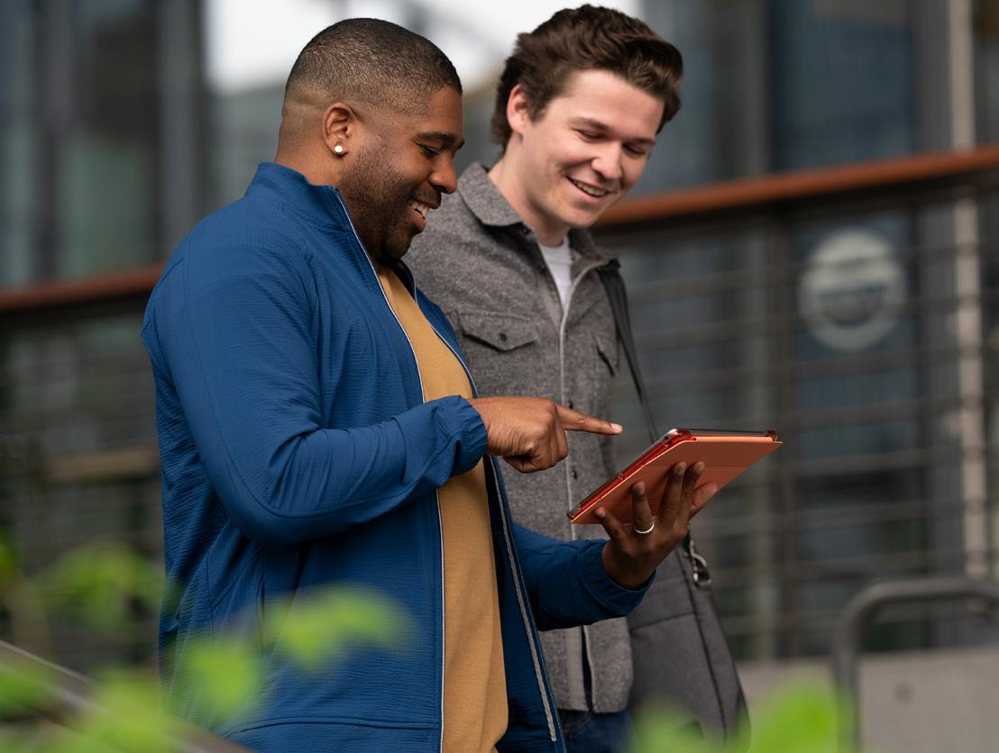 Two builders working in AWS Infrastructure Services view a tablet together outside an AWS office.